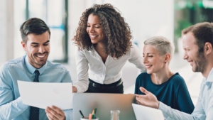 Consultoria de RH: mulher em pé apresentando um projeto de consultoria e mais três pessoas sentadas sorrindo.